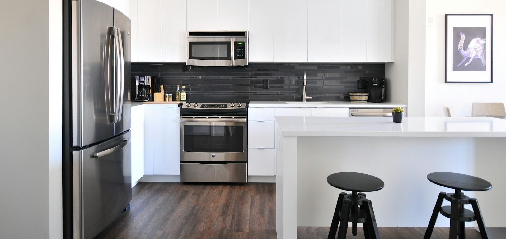 Modern kitchen featuring stainless steel appliances, white cabinets, and dark wood flooring.