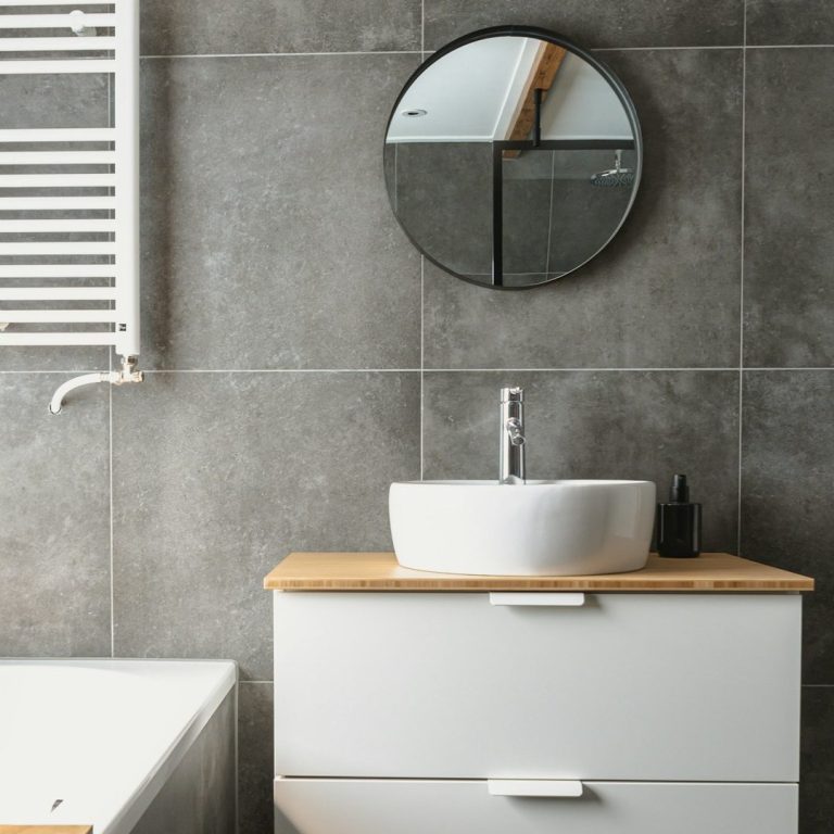 Modern bathroom featuring a circular mirror, white sink, and wooden vanity.