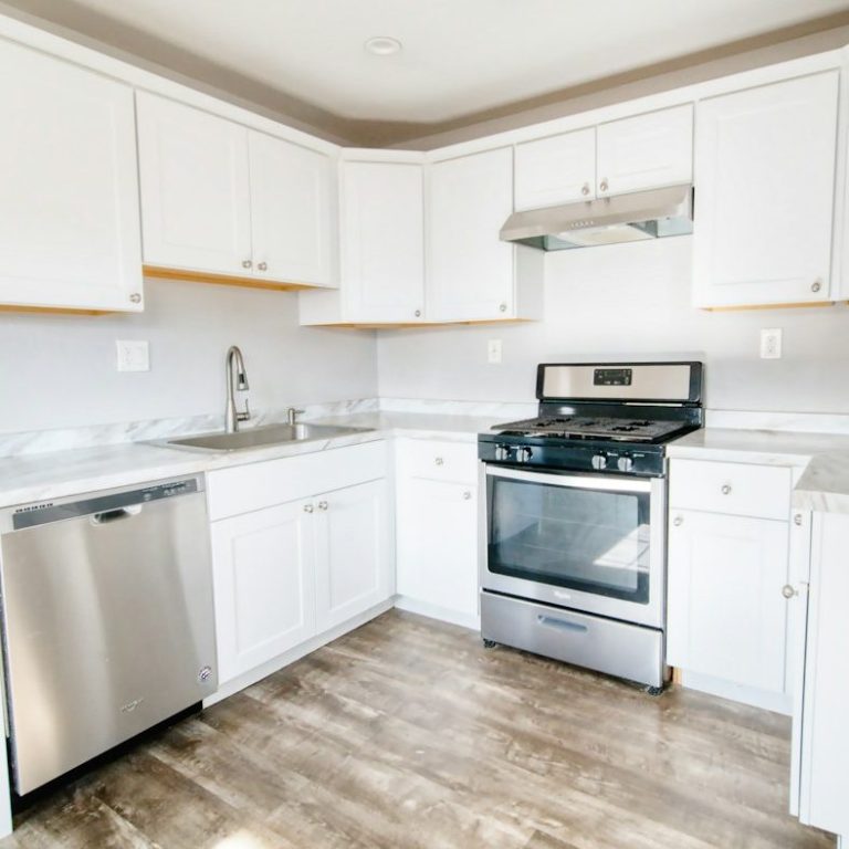 Modern kitchen with white cabinets, stainless steel appliances, and a wooden floor.
