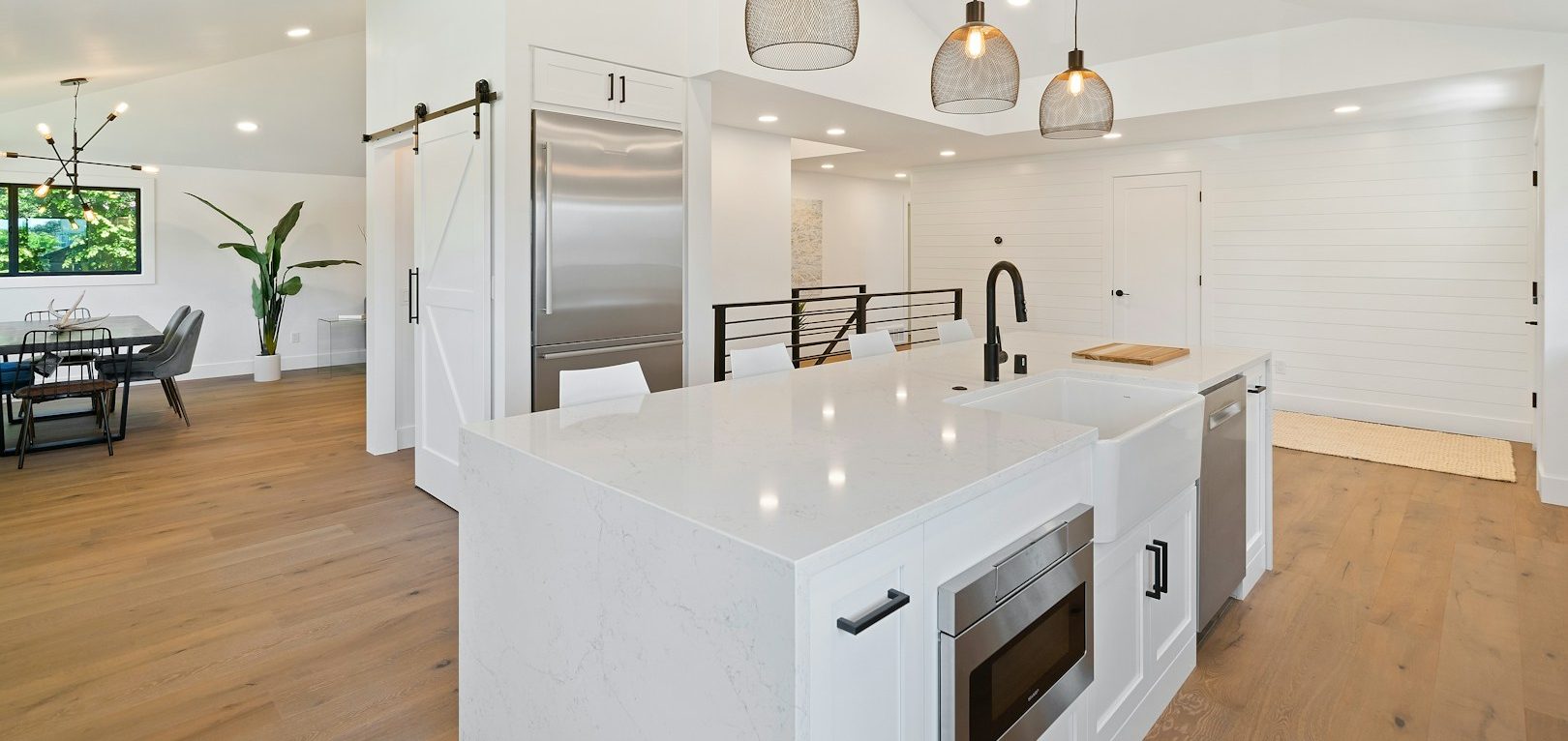 Bright, modern kitchen with white cabinetry, island, and wood flooring. Light fixtures above.
