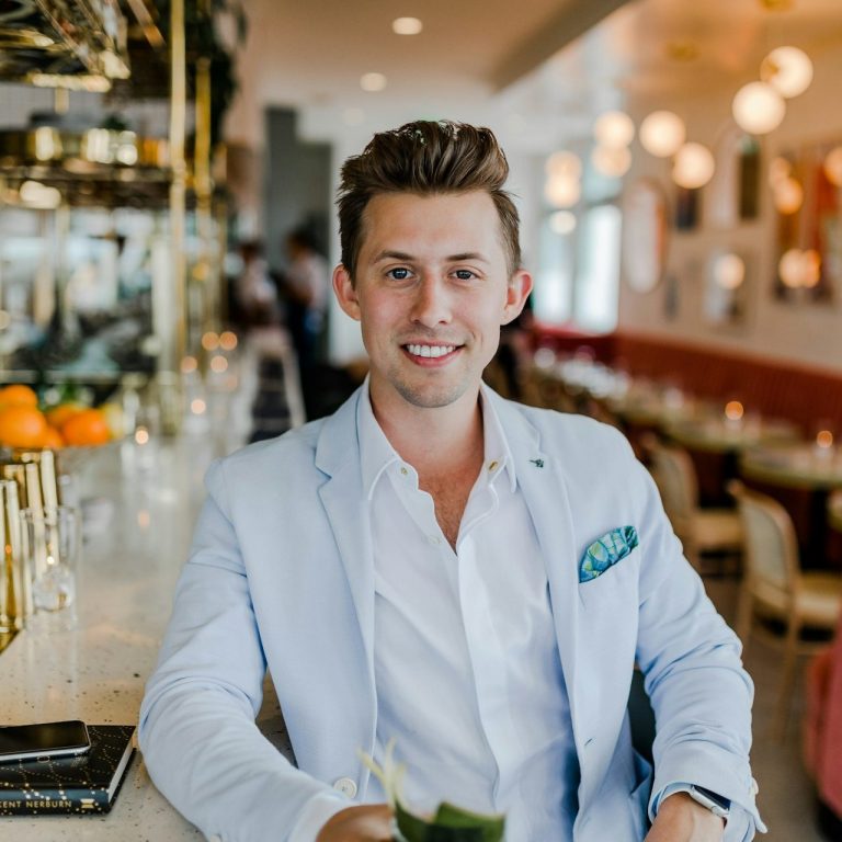 Young man in a light blazer holding a cocktail, smiling in a modern bar setting.